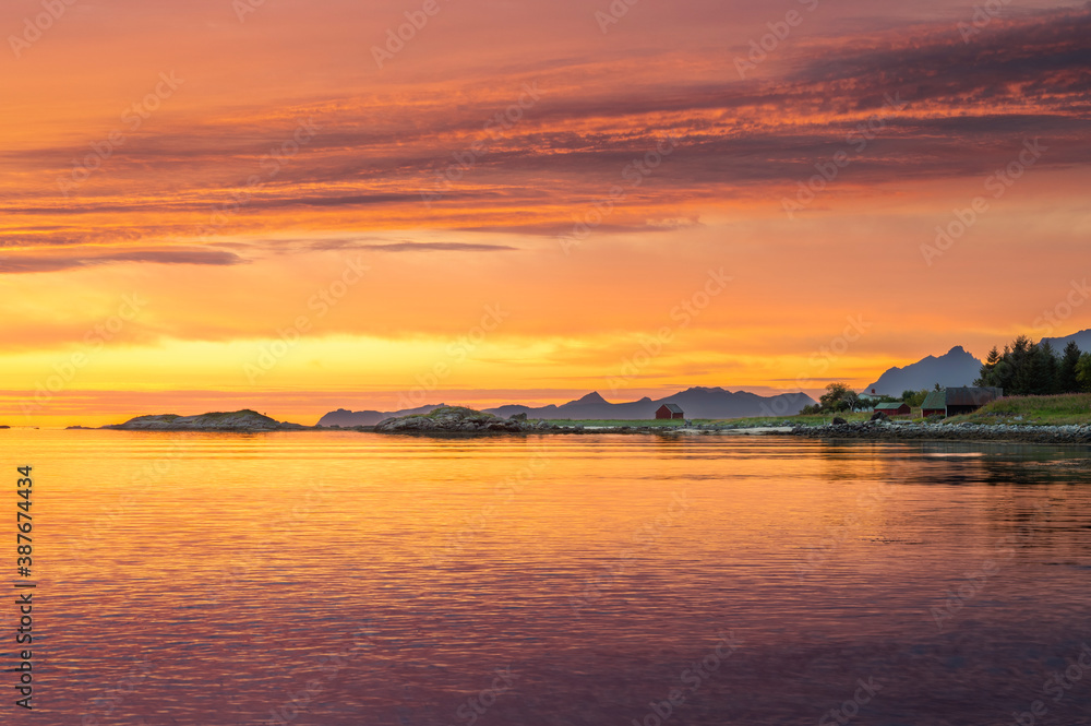 Colourful sunset over Norwegian fjords in Lofoten islands  with classic red wooden shed in background.