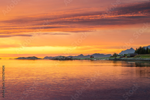 Colourful sunset over Norwegian fjords in Lofoten islands with classic red wooden shed in background.