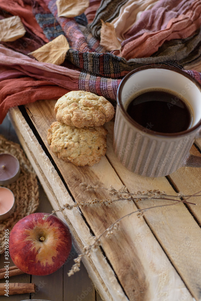 Oatmeal cookies with a mug of black coffee on a wooden box with dried flowers, an apple, candles, an orange-brown scarf Oatmeal cookies with a mug of black coffee on a wooden box with dried flowers, an apple, candles, an orange-brown scarf