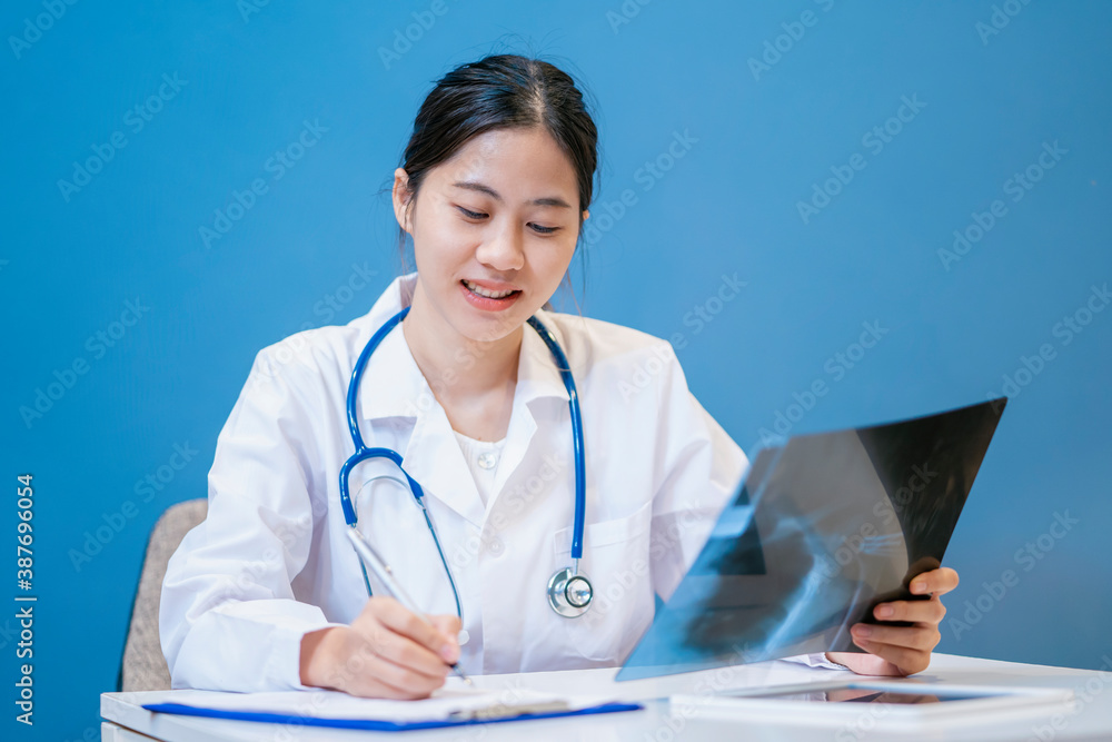 Medical healthcare Asian female attractive doctor showing x-ray film radiograph diagnosing patient health bone shoulder injury, tablet medical technology in hospital office blue isolated background Medical healthcare Asian female attractive doctor showing x-ray film radiograph diagnosing patient health bone shoulder injury, tablet medical technology in hospital office blue isolated background