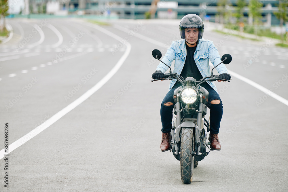 Confident Vietnamese motorcyclist wearing helmet when riding fast on highway