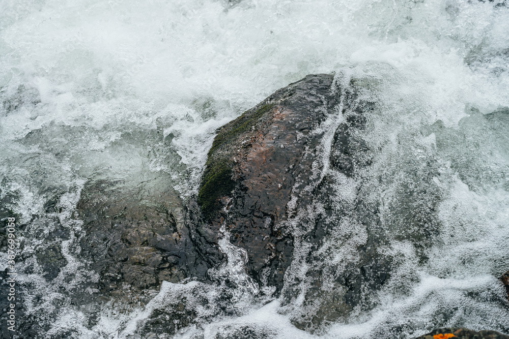 Obraz premium Full frame nature background with boulders in water riffle of mountain river. Powerful water stream of mountain creek. Textured backdrop of fast flow of mountain brook with rapids. Big stones close-up