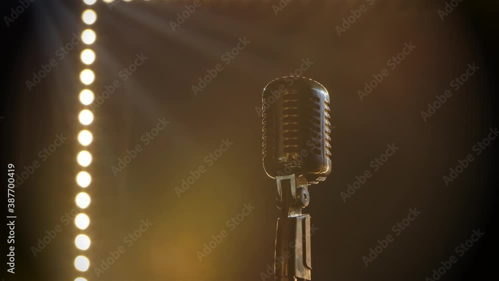 Microphone on stage with smoke anding light behind it. Professional concert vintage glare microphone for record or speak to audience on stage in empty retro club close up.