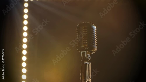 Microphone on stage with smoke anding light behind it. Professional concert vintage glare microphone for record or speak to audience on stage in empty retro club close up.