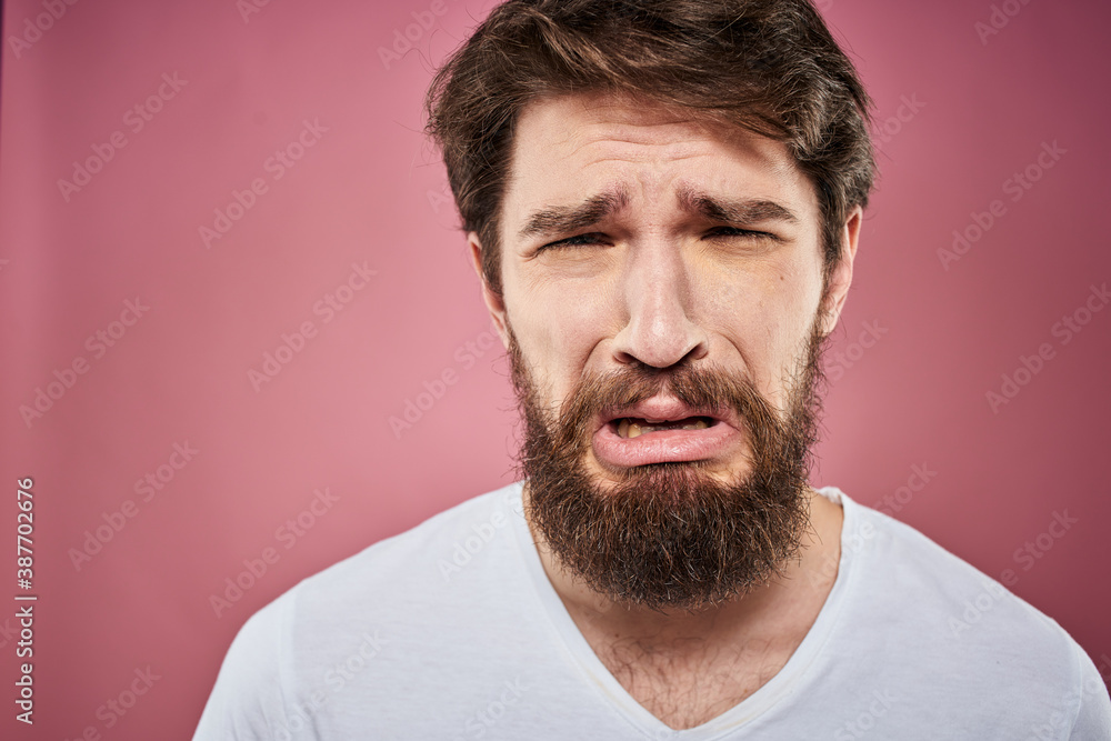 Emotional bearded man in white T-shirt discontent pink background
