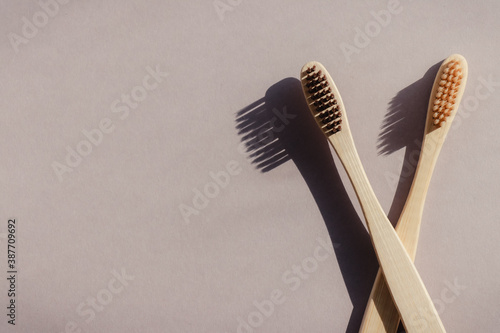 Two biodegradable bamboo toothbrushes on a beige background with contrasting shadows.