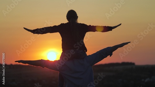 happy dad and little child play, fantasize on plane with child. dream of flying with dad. girl daughter sitting on fathers neck play superhero pilot. silhouette at sunset. happy family resting in park