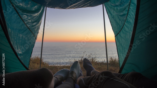 Couple watches the sunrise in the morning when they wake up in a tent camped by the sea