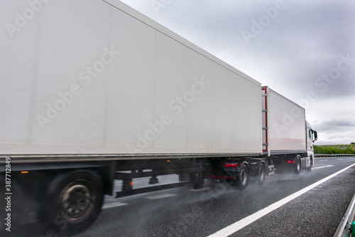 Mega trailer or road train circulating on a day with bad weather due to rain, with the road wet and the wheels raising a cloud of water. © M. Perfectti