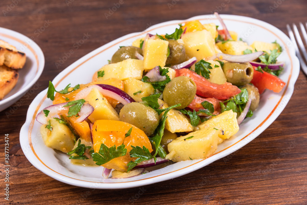 Traditional Italian Calabrian potato salad - oval plate with boiled potatoes, tomatoes, onions and olives on a plain table close-up Traditional Italian Calabrian potato salad - oval plate with boiled potatoes, tomatoes, onions and olives on a plain table close-up