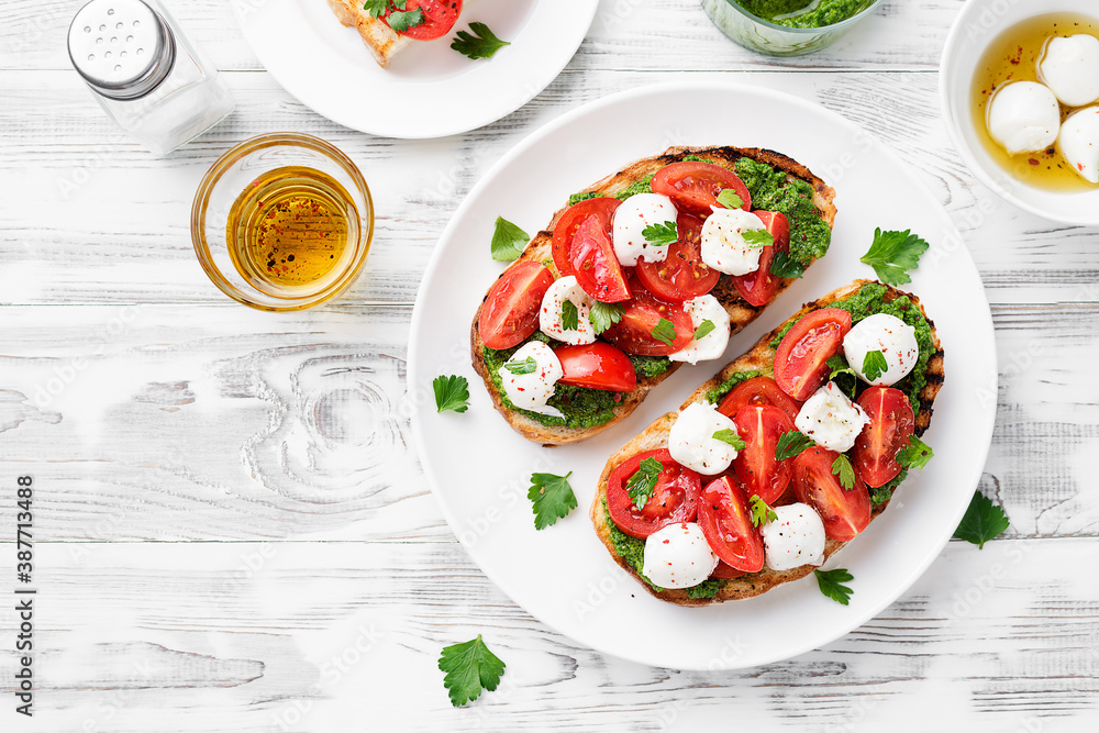 Bruschetta with cherry tomatoes, mozzarella cheese and pesto sauce on wooden board. Traditional italian appetizer or snack, antipasto. Bruschetta with cherry tomatoes, mozzarella cheese and pesto sauce on wooden board. Traditional italian appetizer or snack, antipasto.