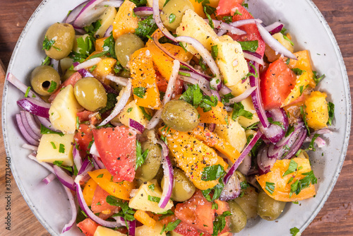 Traditional Italian Calabrian potato salad - a bowl with boiled potatoes, tomatoes, onions and olives on a plain table close-up