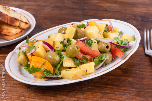 Traditional Italian Calabrian potato salad - oval plate with boiled potatoes, tomatoes, onions and olives on a plain table close-up