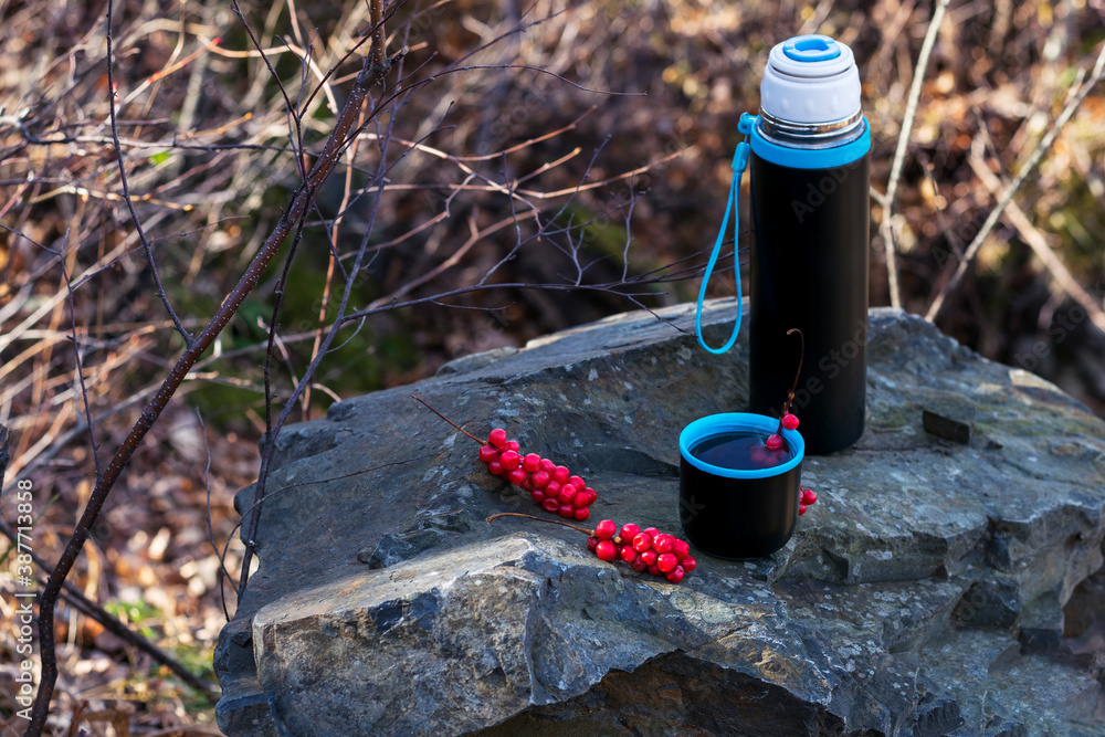 Obraz premium Tourist mug and thermos with tea and lemongrass in nature stands on a stone and green moss.