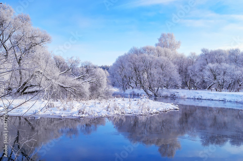 Winter christmas landscape with calm winter river, surrounded by trees.