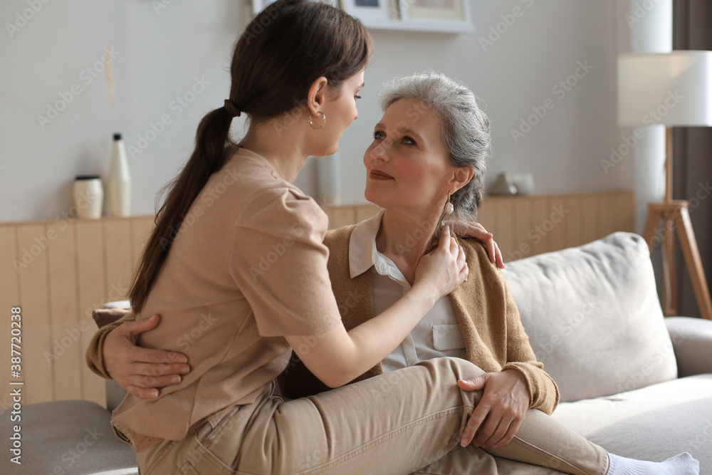 Elderly middle mother sitting on couch with joy holding adult daughter on knees. Happy trusted relations. Family concept.