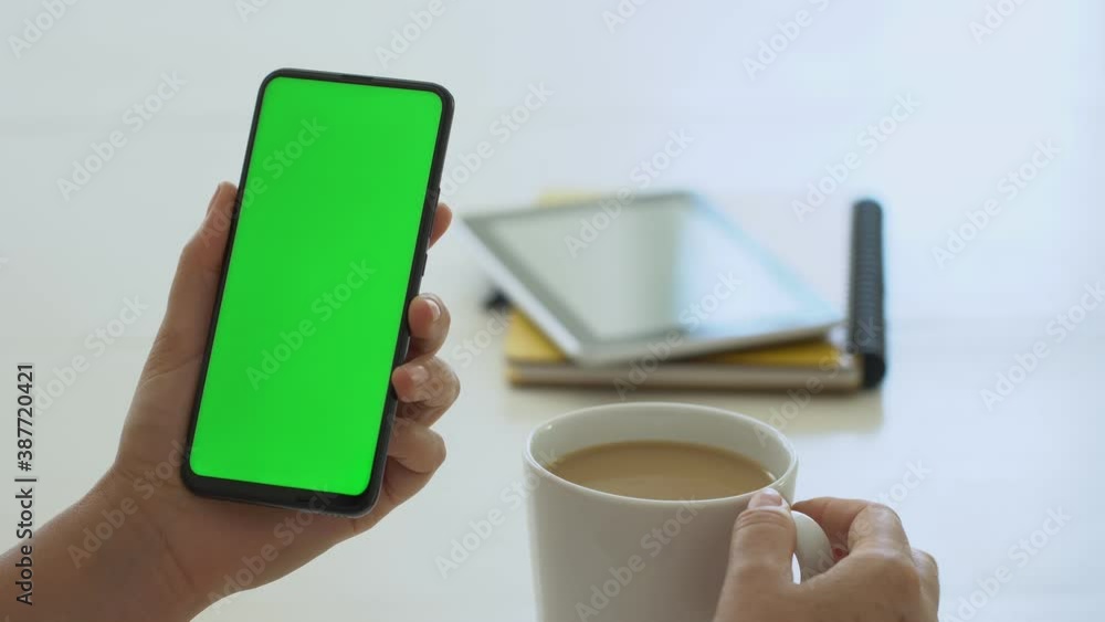 Handheld Camera: business woman using smartphone viewing green screen on mobile phone browsing chroma key online watching enjoying drinking coffee reading social media close up hands Handheld Camera: business woman using smartphone viewing green screen on mobile phone browsing chroma key online watching enjoying drinking coffee reading social media close up hands