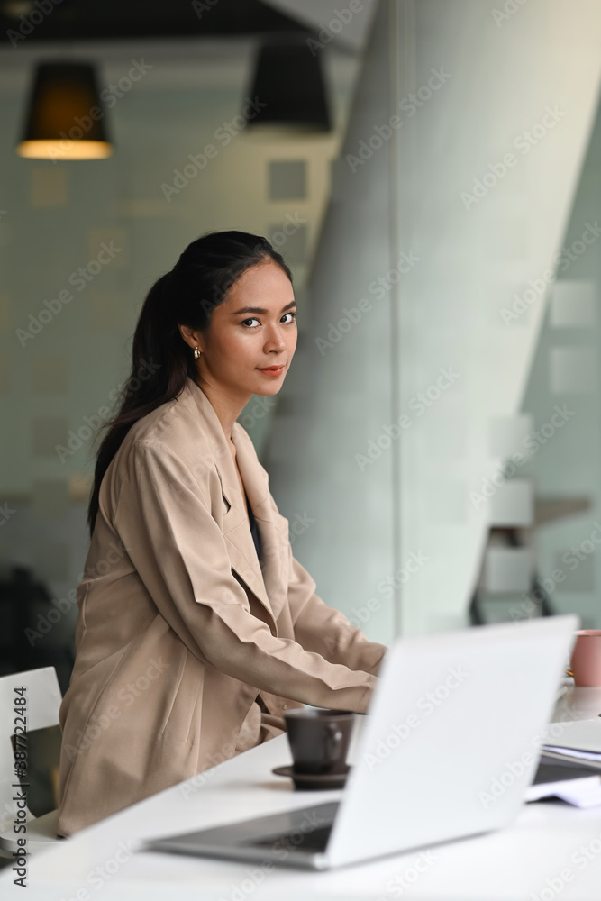 An attractive young businesswoman sitting in her workspace at office and looking at camera. An attractive young businesswoman sitting in her workspace at office and looking at camera.