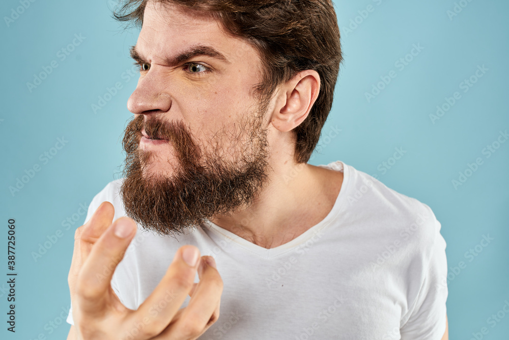 Fototapeta premium Bearded man in white T-shirt emotions gestures with hands displeased facial expression blue background