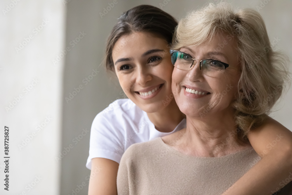 Smiling senior mother and adult daughter hug cuddle look in distance dream think of happy future. Optimistic mature mom and grownup girl child embrace visualize at home, enjoy tender family moment. Smiling senior mother and adult daughter hug cuddle look in distance dream think of happy future. Optimistic mature mom and grownup girl child embrace visualize at home, enjoy tender family moment.