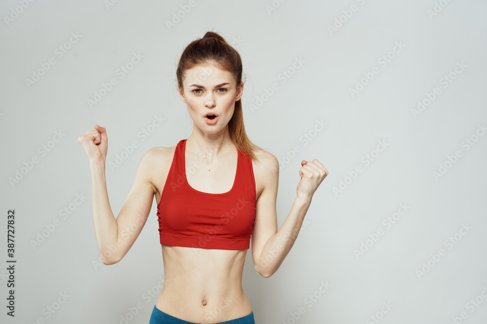 A woman in a red T-shirt on a light background is engaged in fitness gestures with her hands a slim figure  - obrazy, fototapety, plakaty 