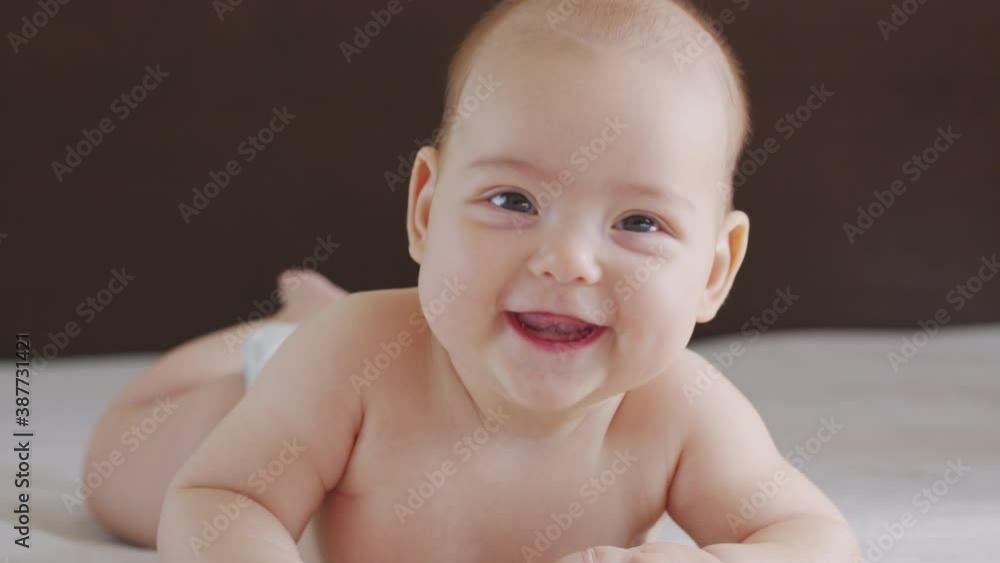 Beautiful Smiling Baby: A gorgeous little baby lies on the bed and smiles at the camera with a nice soft focus background. Beautiful Smiling Baby: A gorgeous little baby lies on the bed and smiles at the camera with a nice soft focus background.