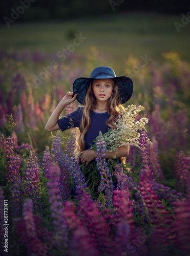 Obraz na płótnie Happy young girl in blue dress and hat with violet flowers in the summer blooming field watcing at the camera w salonie