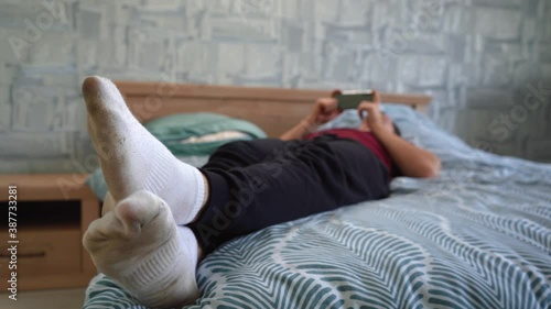 a man in dirty white socks is lying on the bed and playing on the phone