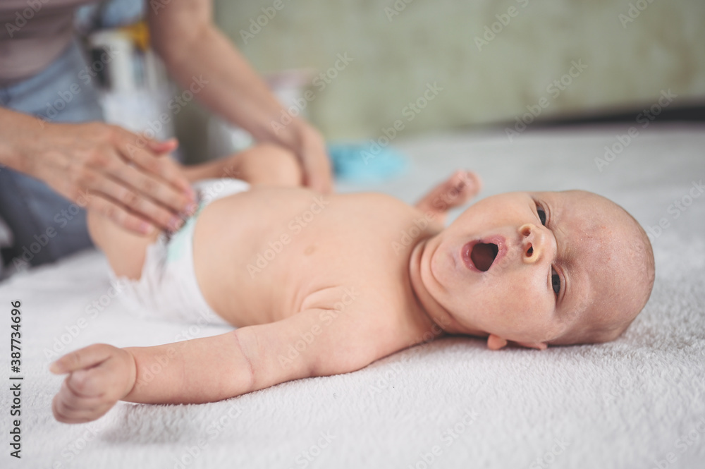 Mother is changing diaper for cute emotional funny newborn little infant baby boy laying in crib Mother is changing diaper for cute emotional funny newborn little infant baby boy laying in crib