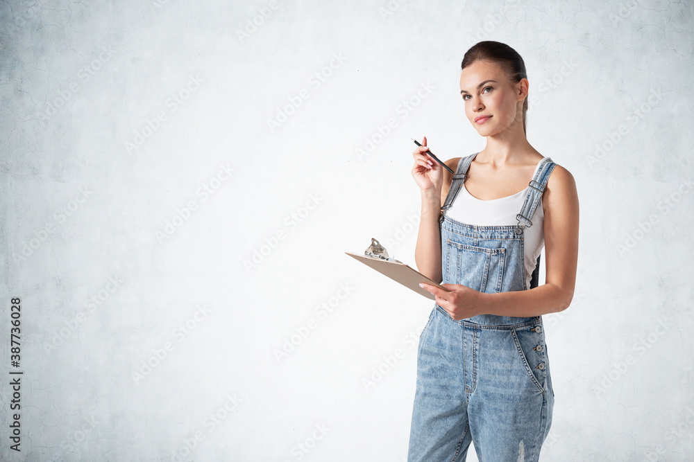 Beautiful young woman in overalls with clipboard