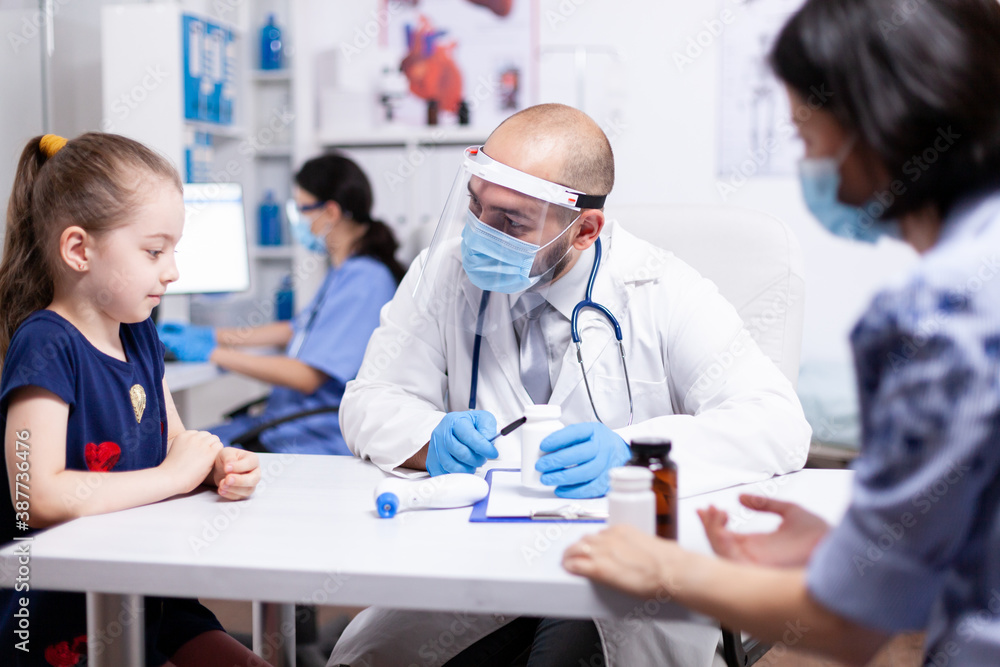 Pediatrician doctor examining sick child in hospital office during covid-19. Health pediatrician specialist providing health care services consultations treatment in protective equipment for