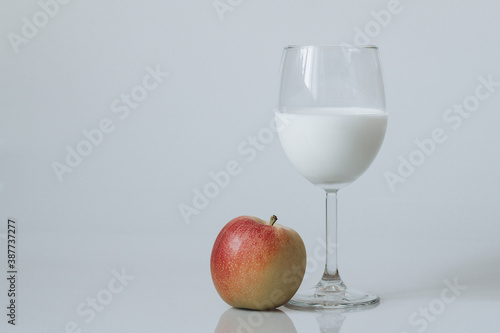 Image of a glass of white drink and red apple on a white background
