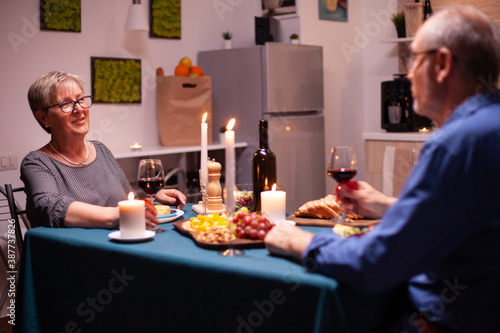 Elderly aged couple celebrating relationship during romantic dinner. Senior couple sitting at the table in kitchen  talking  enjoying the meal in dining room.