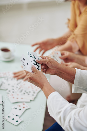 Hands of senior women playing cards and drinking tea when spending weeend together