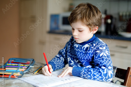 Lonely school kid boy at home making homework. Little child writing with colorful pencils, indoors. Elementary school and education. Home schooling during corona virus pandemic lockdown