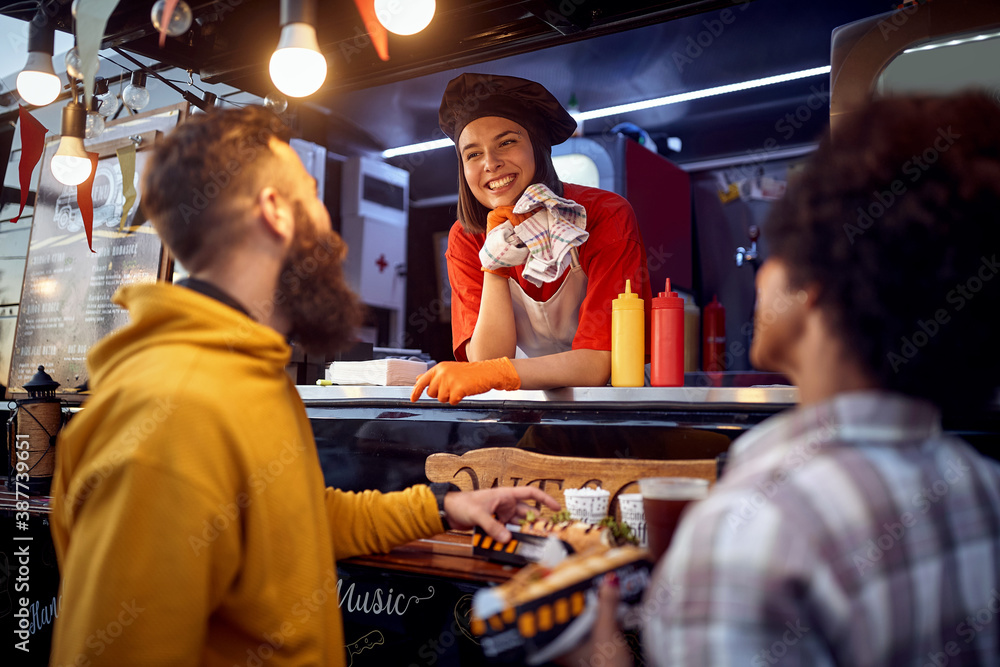 young male is about to eat sandwich in front of fast food service, looking at satisfied employee smiling