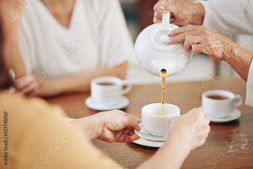 Hands of senior woman pouring hot tea in cups of her guests at party
