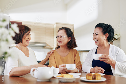 Group of happy senior women drinking tea  eating cakes and discussing news at home
