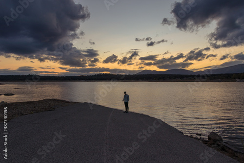 Hombre fotografiando el atardecer desde una carretera que acaba en un lago