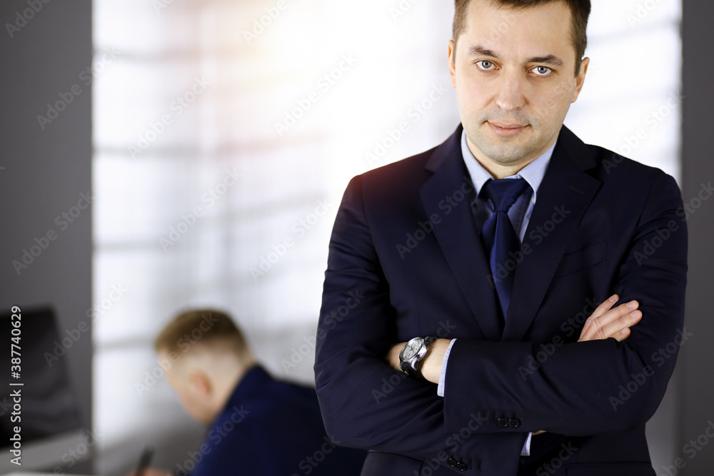 Portrait of a friendly middle aged businessman with crossed arms, while standing in a sunny office. Business concept Portrait of a friendly middle aged businessman with crossed arms, while standing in a sunny office. Business concept