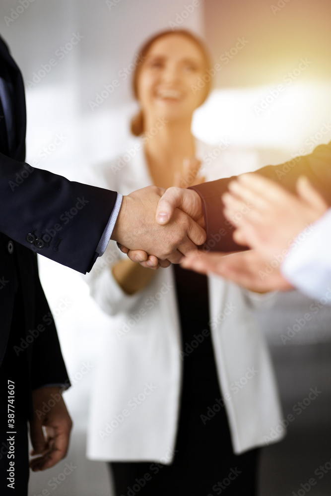 Obraz premium Unknown businesspeople are shaking their hands after signing a contract, while standing together in a sunny modern office, close-up. Business communication, handshake, and marketing concept