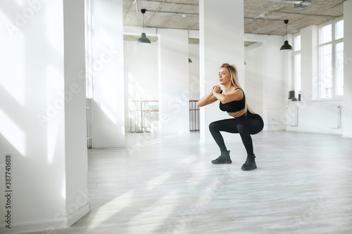 young sportive woman doing squats in the gym. blonde is engaged in a light room