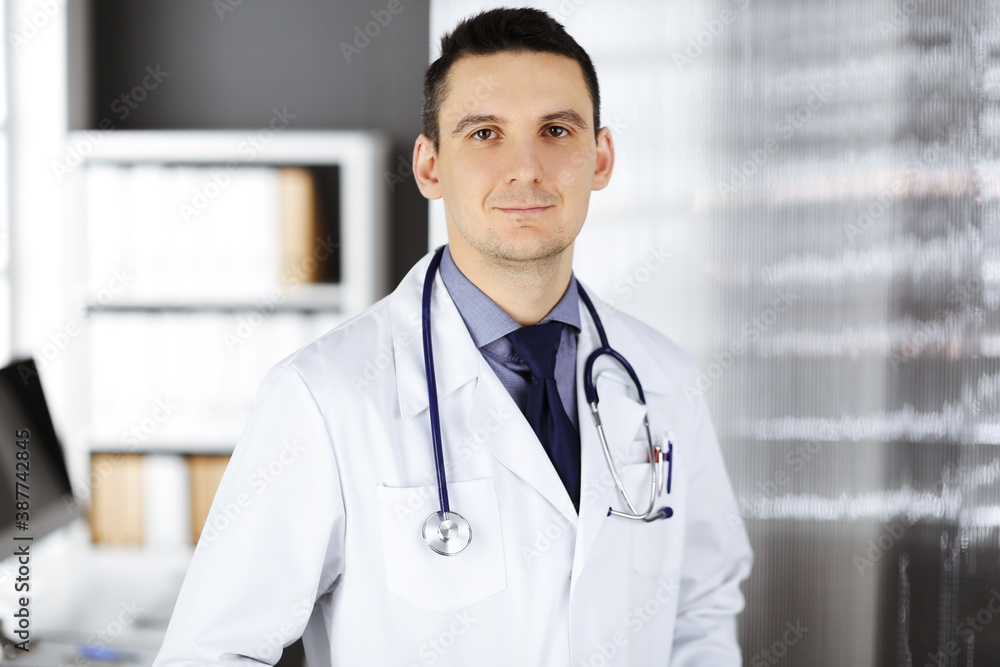 Male doctor standing straight in clinic near his working place. Perfect medical service in hospital. Medicine and healthcare concept Male doctor standing straight in clinic near his working place. Perfect medical service in hospital. Medicine and healthcare concept