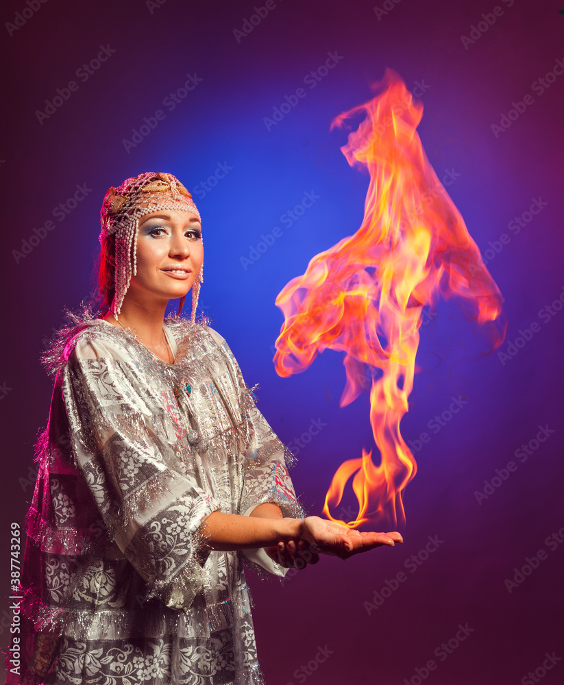 Fairy in a white festive new year costume lights a flame on her hand in the studio