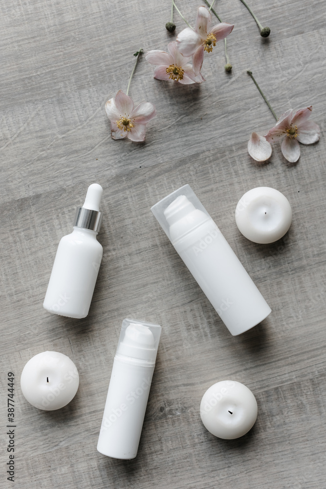 white bottles for cream and serum on a gray table with round candles white bottles for cream and serum on a gray table with round candles