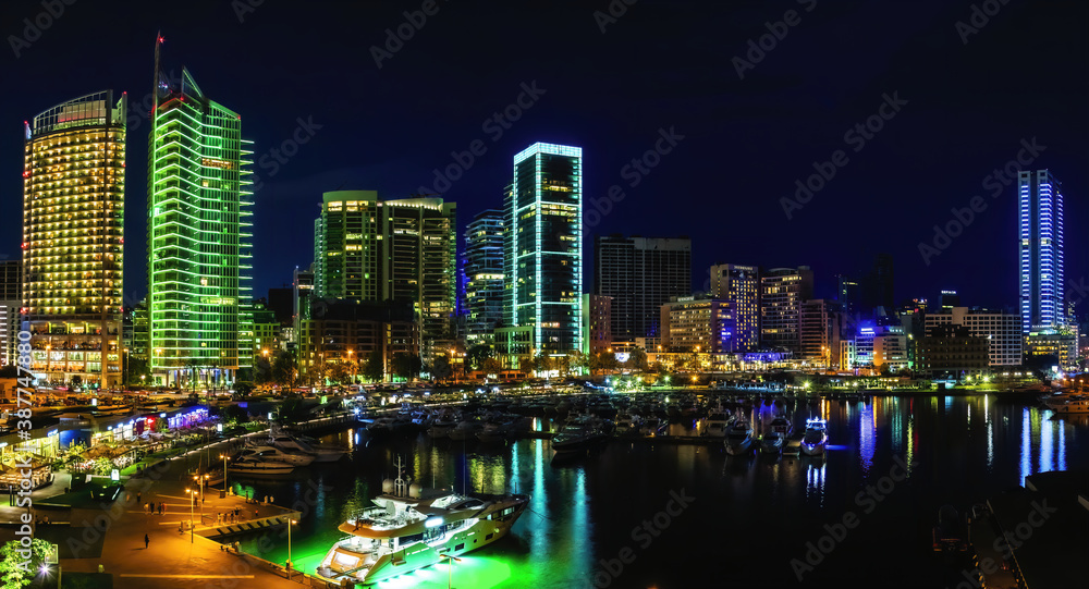 Obraz premium A panoramic photo of Beirut, Lebanon city skyline at night, featuring the vibrant neon lights of the marina with boats and a scenic waterfront walk. 