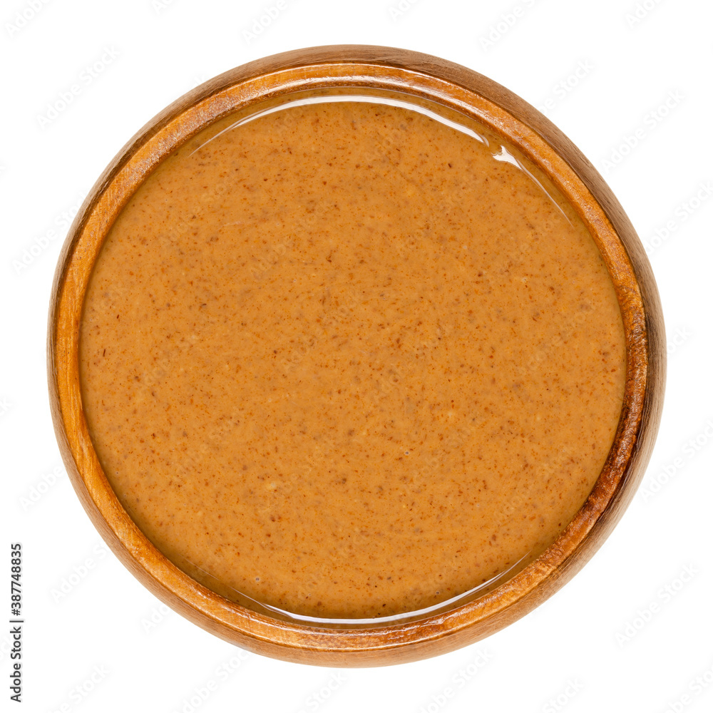 Smooth almond butter in a wooden bowl. Food paste made from grinding almonds into a nut butter. Puree of the nuts of Prunus dulcis. Close-up from above, isolated on white background, macro food photo. Smooth almond butter in a wooden bowl. Food paste made from grinding almonds into a nut butter. Puree of the nuts of Prunus dulcis. Close-up from above, isolated on white background, macro food photo.