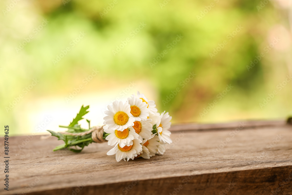 Small bunch of chrysanthemum flowers tied with brown string on wooden surface with green bokeh background