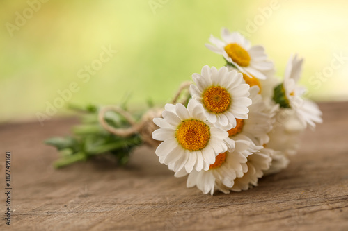 Small bunch of chrysanthemum flowers tied with brown string on wooden surface with green bokeh background © Caseyjadew