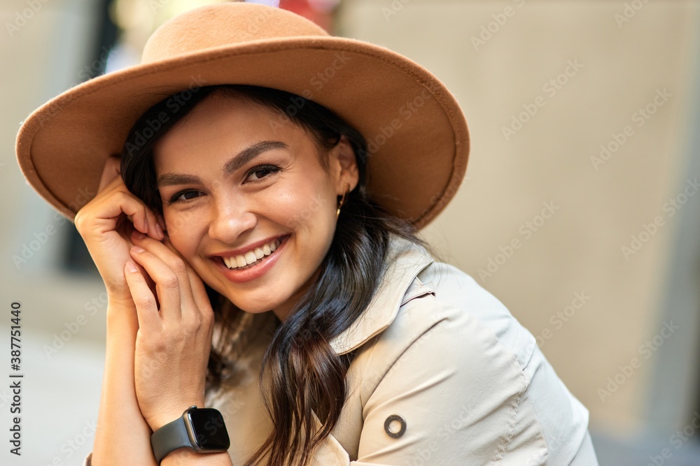 Portrait of a young cute happy woman wearing hat looking at camera and smiling while spending time outdoors - obrazy, fototapety, plakaty 